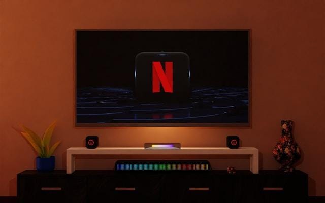A flatscreen TV displaying the Netflix logo, hanging on an orange wall. 