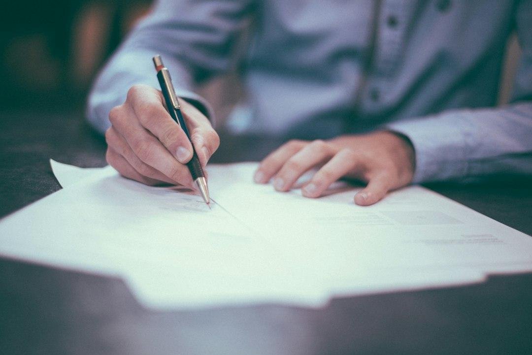 A person signing a printed document with a pen at a desk