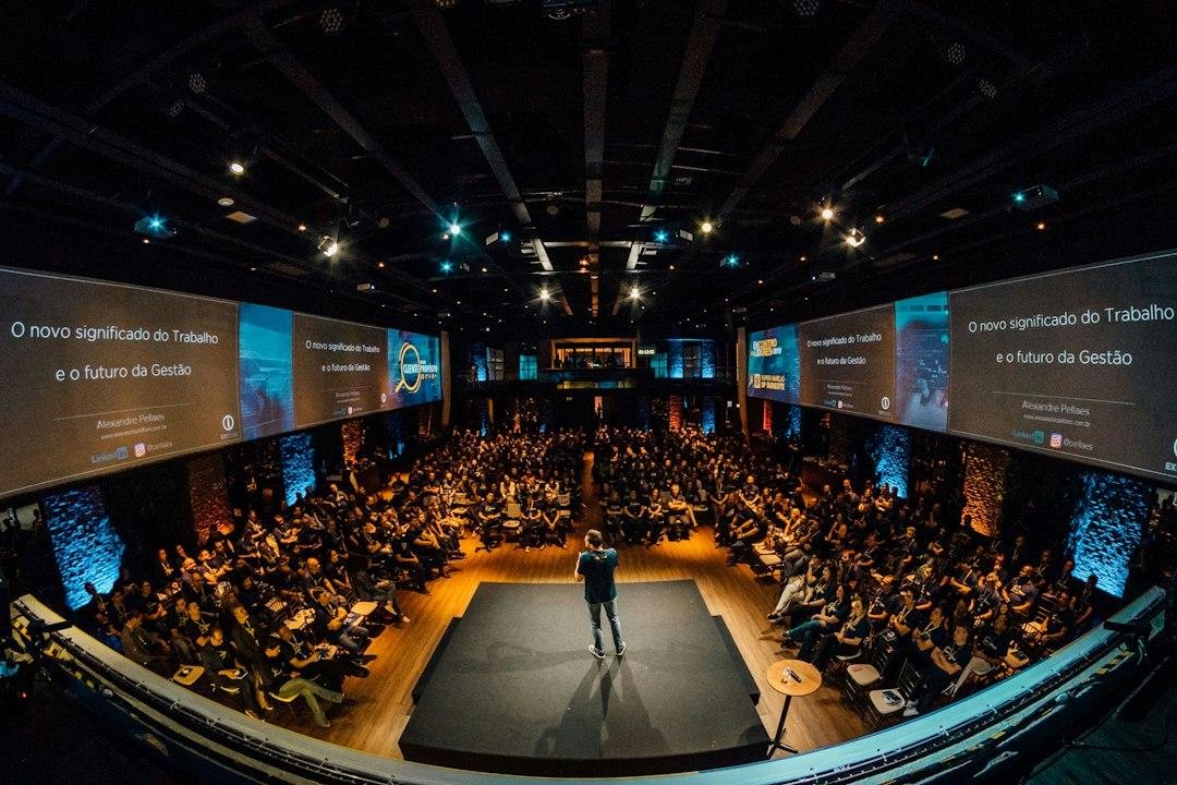 A speaker on a conference stage in front of a large seated audience